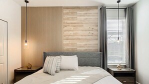 Une chambre moderne avec un grand lit, un mur recouvert de panneaux en bois et une fenêtre avec des rideaux.