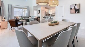 Uma sala de estar moderna com área de jantar, janelas amplas e uma cozinha ao fundo.