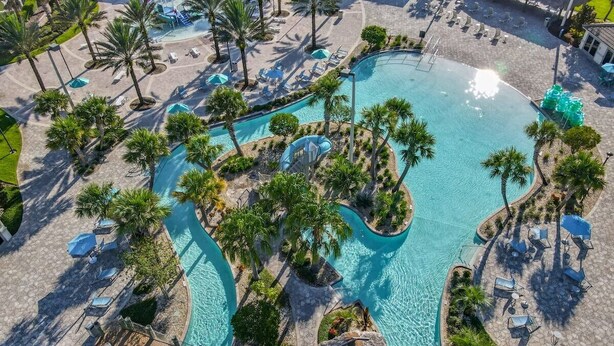 Vista aérea de um resort com piscina central, palmeiras, áreas de descanso e uma ponte.