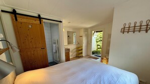 A bedroom with a large bed, a wooden door, a white radiator, a small window, and a wall-mounted towel rack.