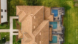 An aerial view of a modern house with a unique geometric roof design, a swimming pool, and a well-maintained lawn. - Last Minute Disney Getaway! Private Pool & Themed Bedrooms. Book Now! #114191 (Orlando)