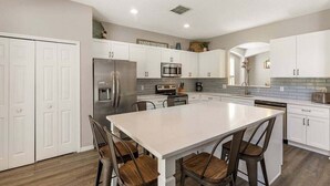 A modern kitchen with white cabinetry, stainless steel appliances, and a large island with bar stools. - Last Minute Disney! Private Pool, Hot Tub, Game Room & Themed Bedrooms. Book Now! #113671 (Orlando)