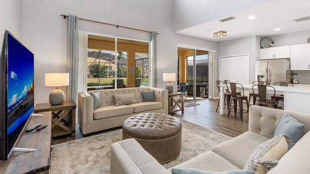 A spacious living area with a sofa, ottoman, and a flat-screen TV. - Last Minute Disney! Private Pool, Hot Tub, Game Room & Themed Bedrooms. Book Now! #113671 (Orlando)
