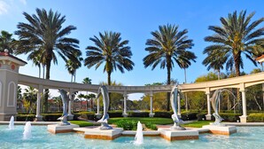 A fountain with dolphin sculptures in a pool, surrounded by palm trees and a pavilion with the text "MERALD ISLAND". - Last Minute Disney! Private Pool, Hot Tub, Game Room & Themed Bedrooms. Book Now! #113671 (Orlando)