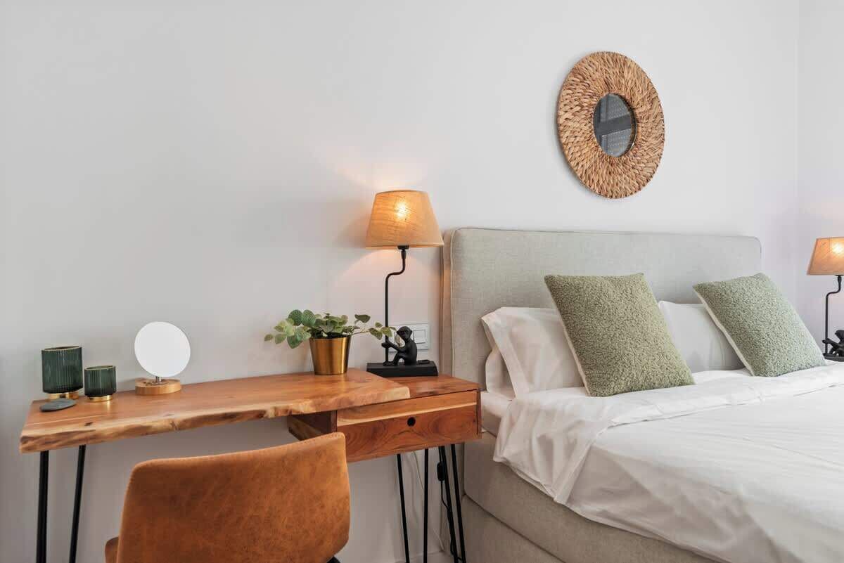 A bedroom with a bed, a desk, a chair, a lamp, a mirror, and a wall decoration.