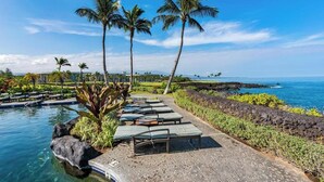 A poolside area with lounge chairs, palm trees, and a view of the ocean.