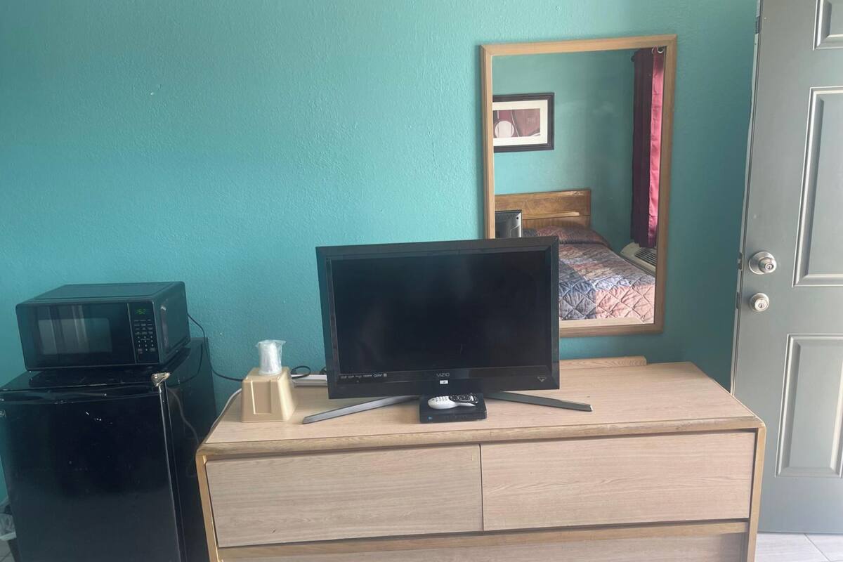 A bedroom with a bed, a TV, a microwave, and a small cabinet.