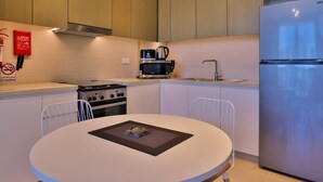 A modern kitchen with wooden cabinets, a stainless steel refrigerator, a stove, a microwave, and a sink. There is a white dining table with chairs and a fire extinguisher on the wall. - One Bedroom Near Dubai Wheel & JBR by Belvilla (Dubai)