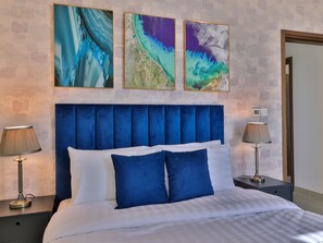 A hotel room with a large bed, two bedside tables, and three abstract paintings on the wall.