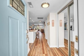 A hallway with wooden flooring, a light blue door, and a kitchen area visible through an open door.
