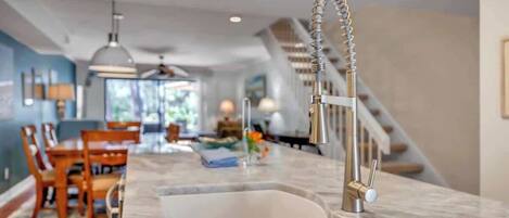 A modern kitchen with a large sink, a dining area with wooden chairs, and a staircase leading to an upper level.