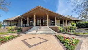 A building with a covered entrance, steps leading up to it, and a landscaped garden area.