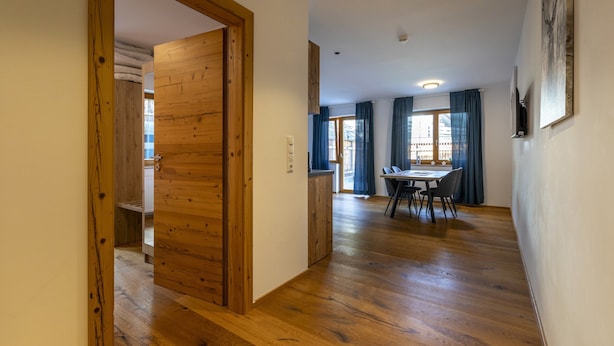 Um quarto espaçoso com piso de madeira, área de jantar com mesa e cadeiras, e vista para o exterior através de uma janela.