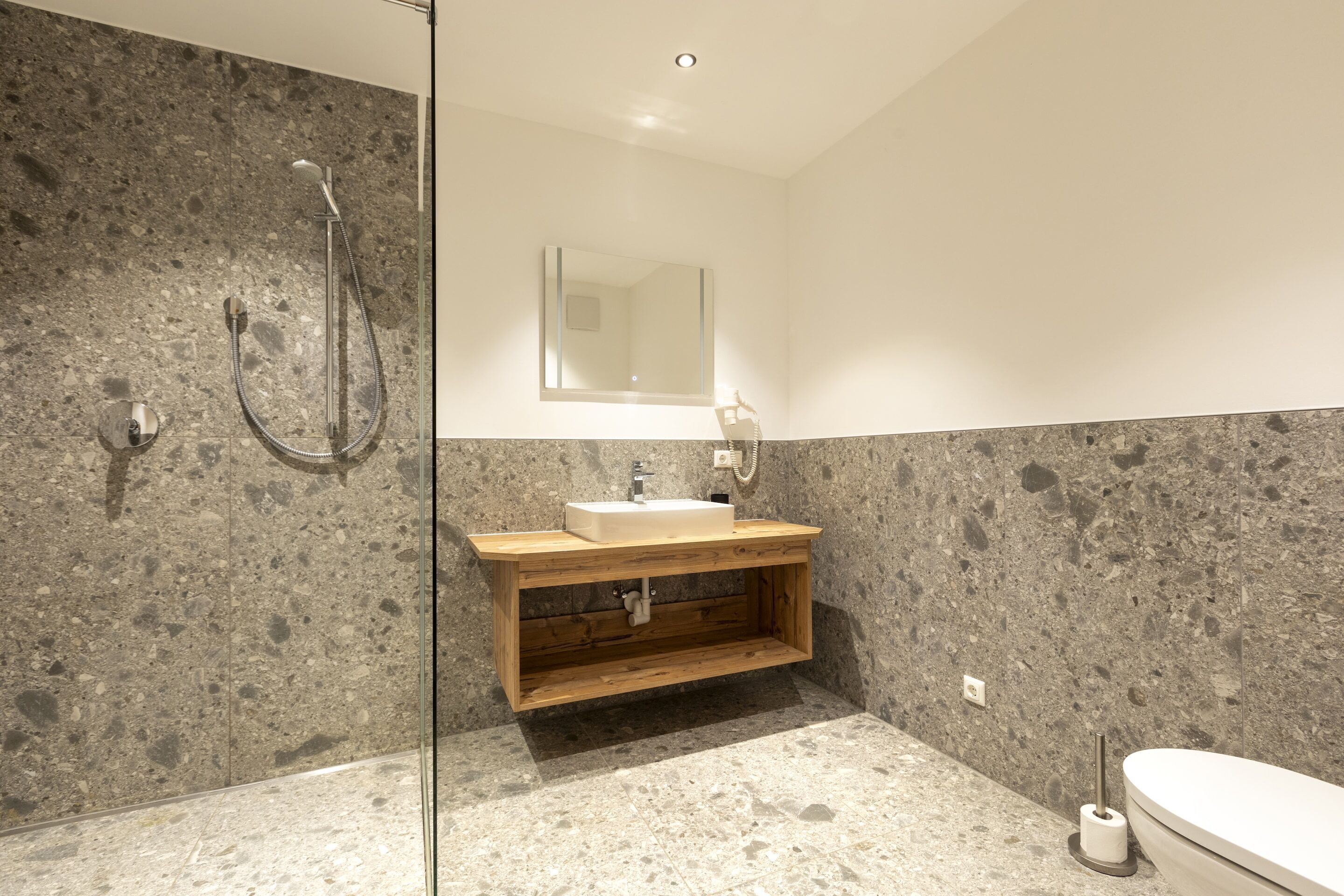 Un baño moderno con ducha independiente, tocador de madera y un espejo grande.