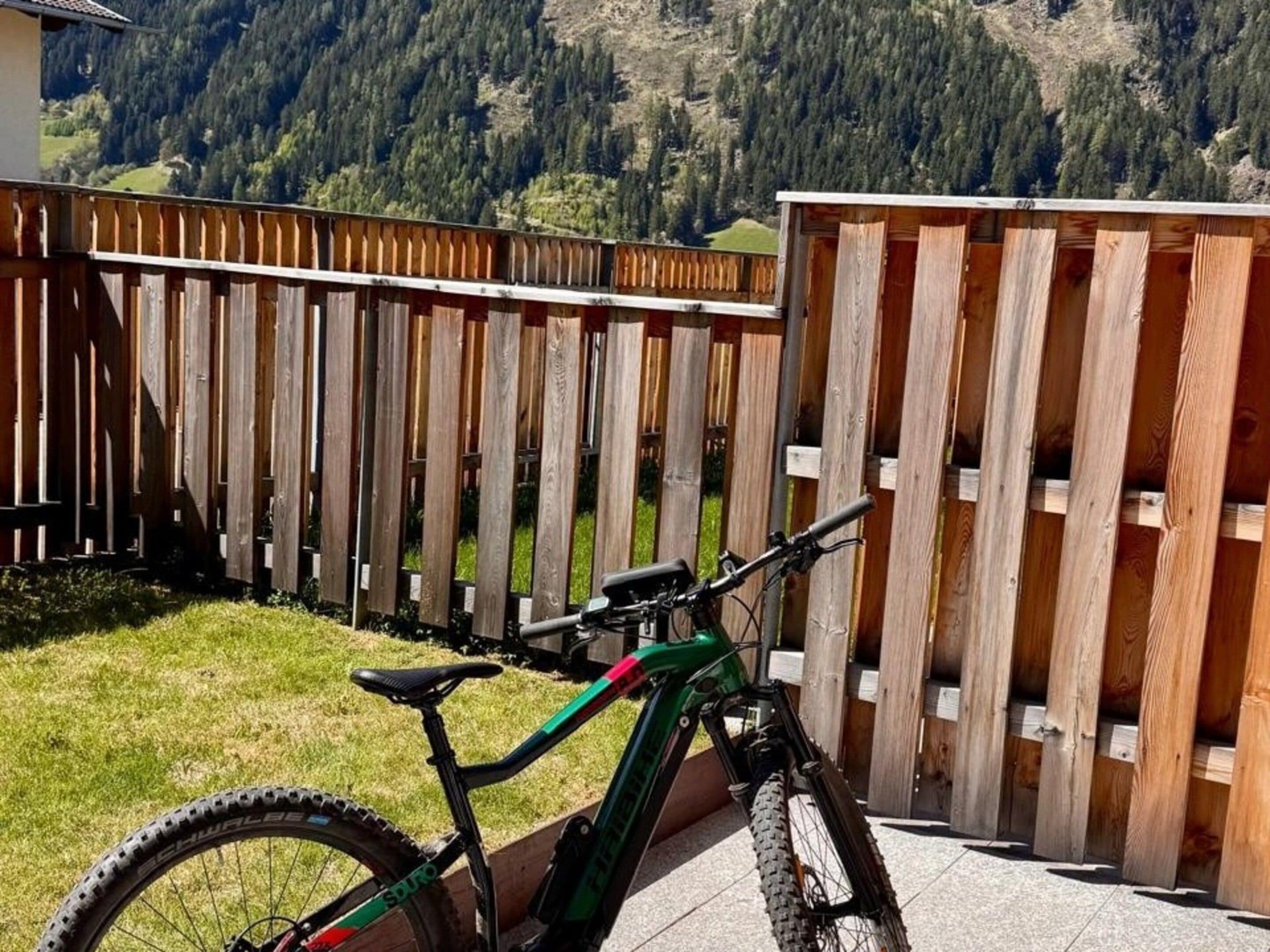 Ein Fahrrad steht in einem umzäunten Außenbereich mit Blick auf eine gebirgige Landschaft.
