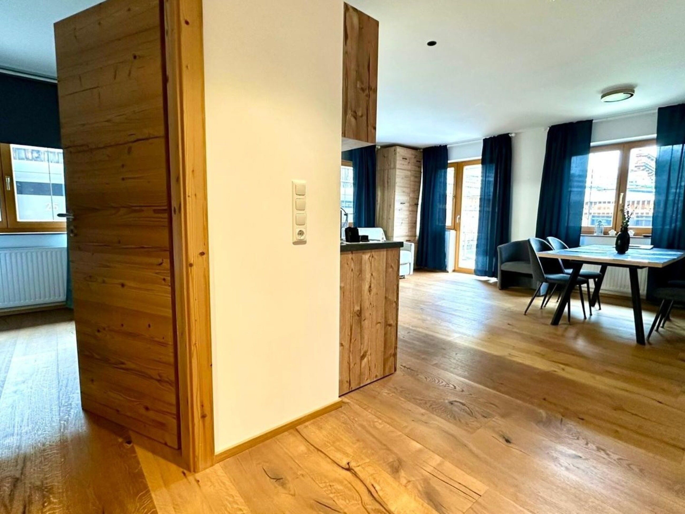 A modern interior with a wooden partition, a dining area with chairs, and a window with curtains.