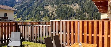 Eine Terrasse im Freien mit Holztisch und -stühlen, einem Holzzaun und Blick auf die Berge im Hintergrund.