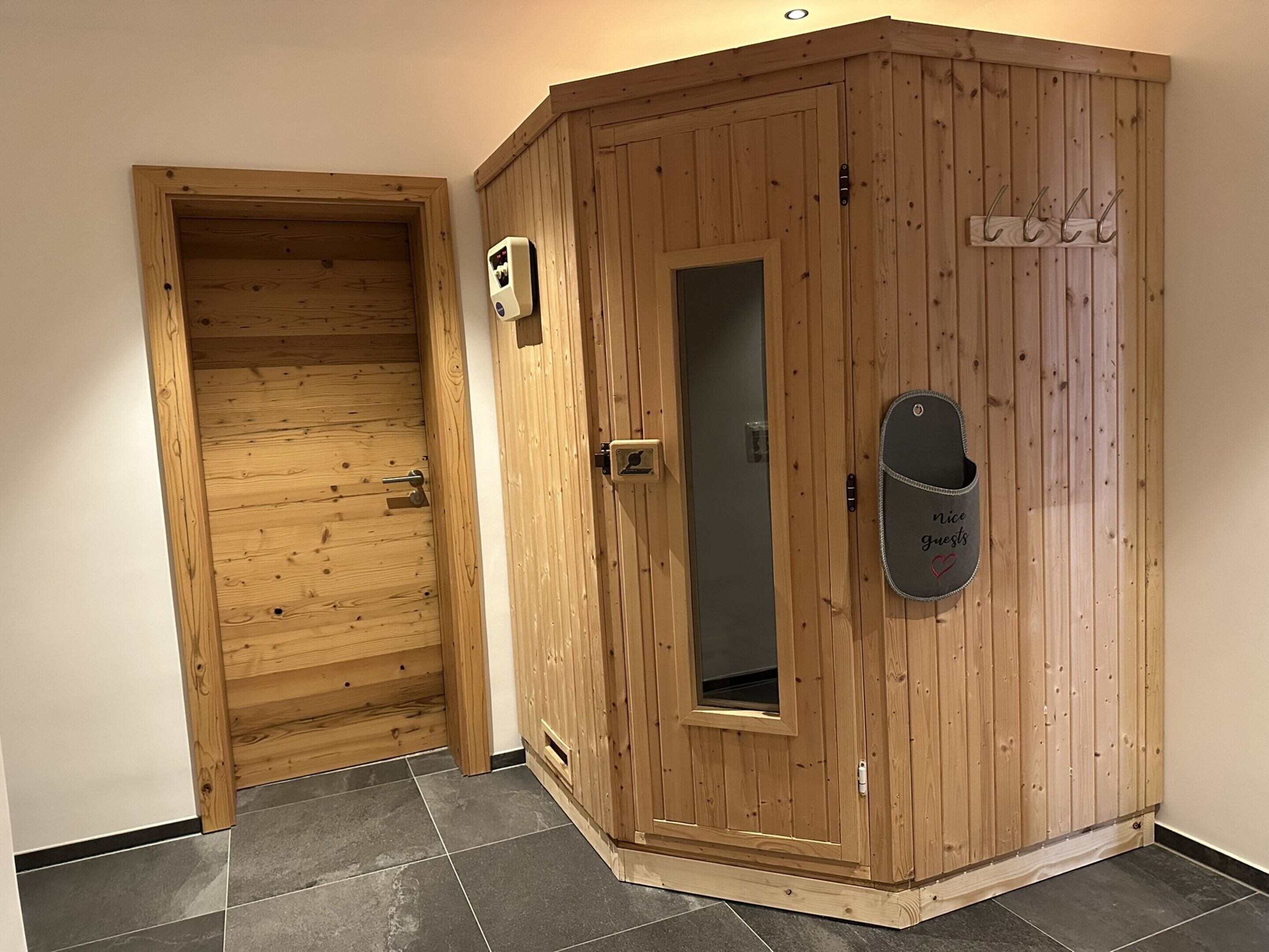 A wooden sauna with a door, a window, and a towel rack.