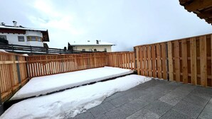 A rooftop terrace with a wooden fence, snow-covered ground, and a view of buildings in the background.
