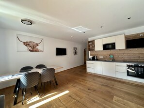 A modern kitchen with wooden cabinets, a built-in oven, and a dining area with a table and chairs. - Apartment in Stubaital Near Ski Lift (Neustift Im Stubaital)