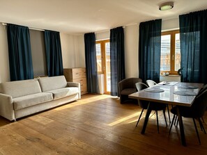 A room with a sofa, a dining table with chairs, a wooden cabinet, and large windows with curtains. - Apartment in Stubaital Near Ski Lift (Neustift Im Stubaital)