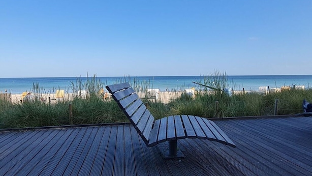 A wooden deck with a bench overlooking a beach. - Holiday Home Apartment - East (Grossenbrode)