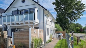 A modern two-story house with a large balcony, a satellite dish, and a well-maintained lawn. - Holiday Home Apartment - East (Grossenbrode)