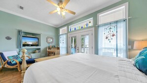 Ein Schlafzimmer mit einem großen Bett, einem Deckenventilator, einem Fernseher, einem Sessel und Blick ins Freie.