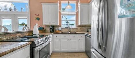 A kitchen with white cabinets, stainless steel appliances, and a window with a view of the sky.
