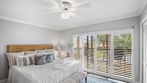 Une chambre avec un grand lit, un ventilateur de plafond et une vue sur l’extérieur, accessible par une porte-fenêtre coulissante.