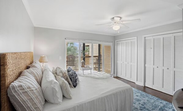 A bedroom with a large bed, white walls, a ceiling fan, and a view through the window.