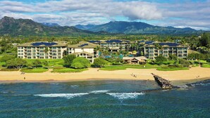 A resort with multiple buildings, a beach, and mountains in the background.