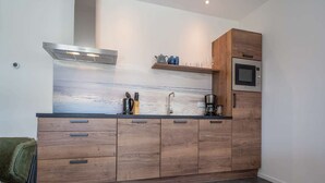 Une cuisine moderne avec des meubles en bois, une hotte de cuisinière en acier inoxydable, un four à micro-ondes encastré et une machine à café.