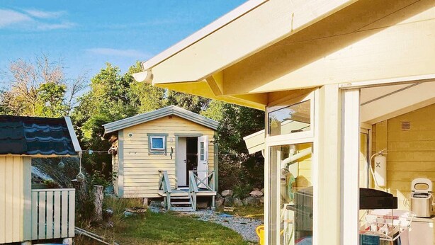 Ein kleines Holzhaus mit einer Veranda, einem bunten aufblasbaren Pool und einer Glastür zu einem Raum mit einer Waschmaschine.