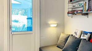 Ein gemütliches Wohnzimmer mit einem grauen Sofa, einem Bücherregal voller Bücher und einem Fenster mit Blick auf eine verschneite Landschaft.
