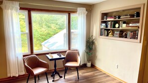 Een kamer met een schaakbord, twee stoelen, een boekenkast en een raam met gordijnen.