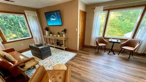 Een ruime woonkamer met een groot raam, een flatscreen televisie, een houten salontafel en lederen fauteuils.