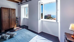 A bedroom with a large window, wooden ceiling beams, a bed, a wardrobe, and a lamp.