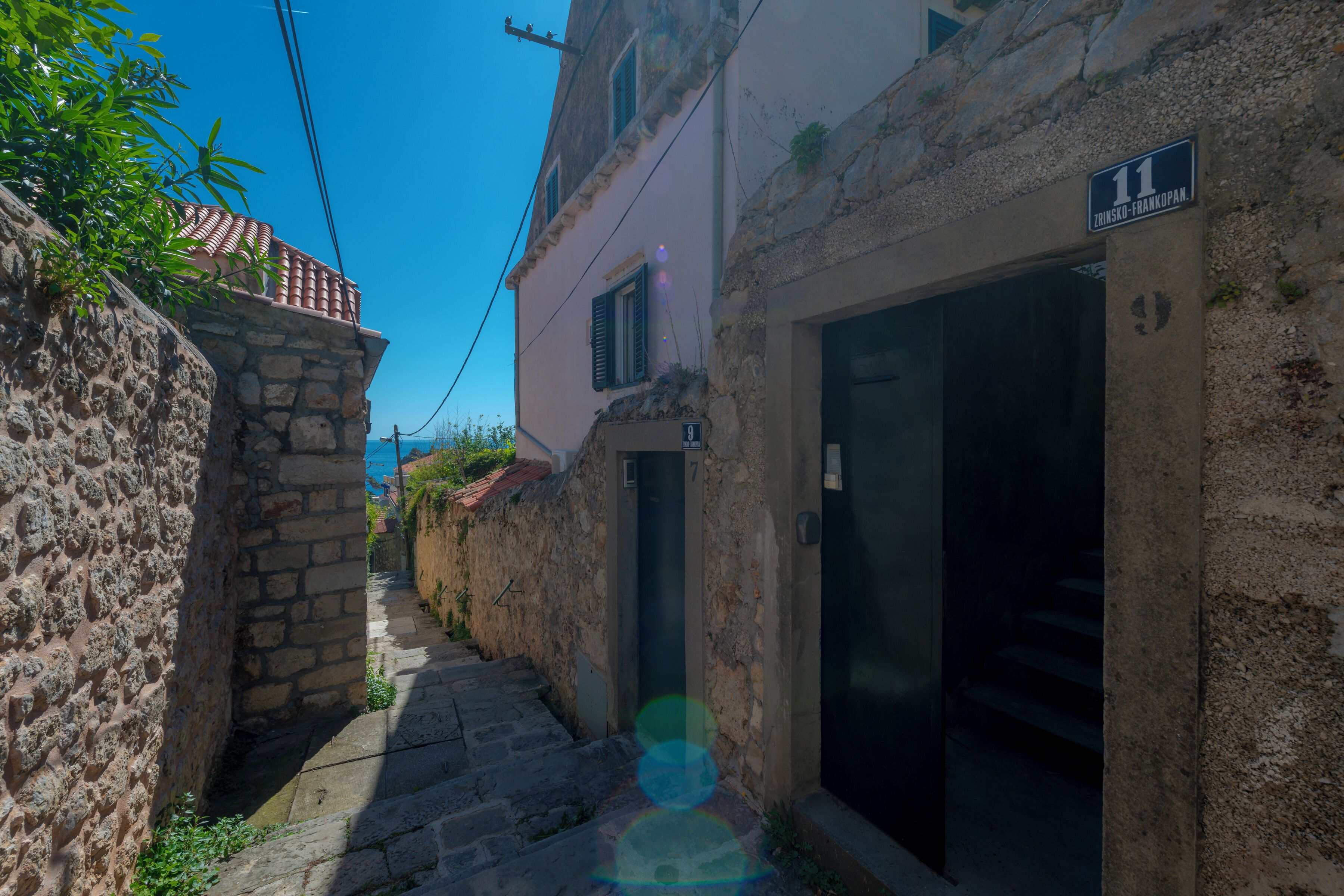 Un estrecho callejón con un muro de piedra a un lado y un edificio con un letrero que indica la habitación número 11.