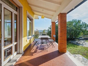 A covered patio with a table and chairs, a yellow wall, and a view of greenery and hills.