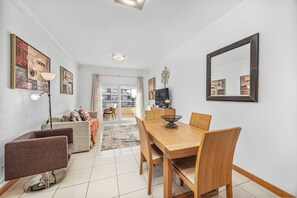 A modern dining area with a wooden table and chairs, a TV, and artwork on the walls. - Pool and Sea View Apartment in Exclusive Condominium (Albufeira)