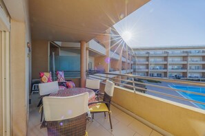 A balcony with a table and chairs, a pool, and a building with multiple balconies in the background. - Pool and Sea View Apartment in Exclusive Condominium (Albufeira)
