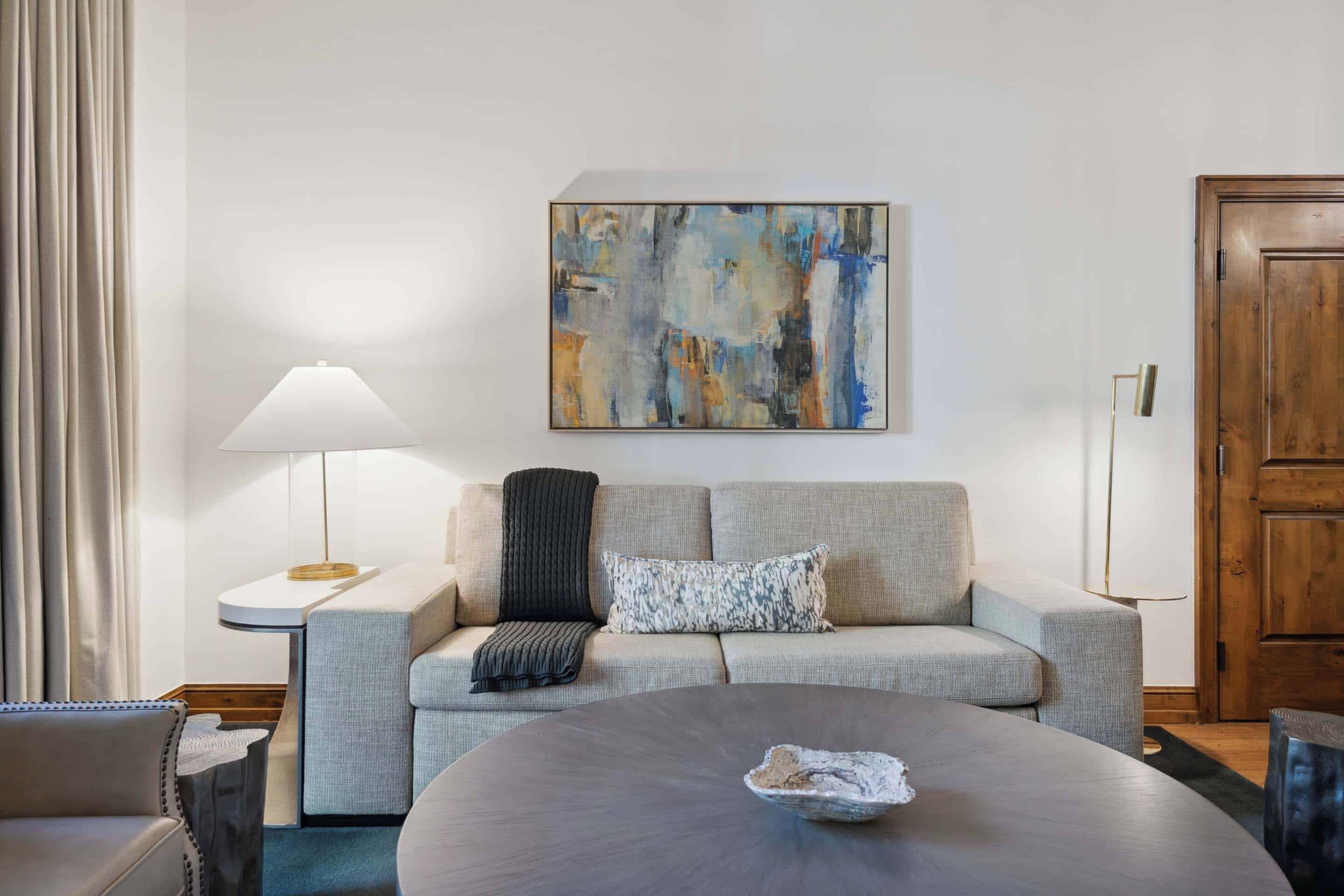 Uma sala de estar moderna com um sofá, uma mesa de centro redonda, uma luminária e um quadro na parede.