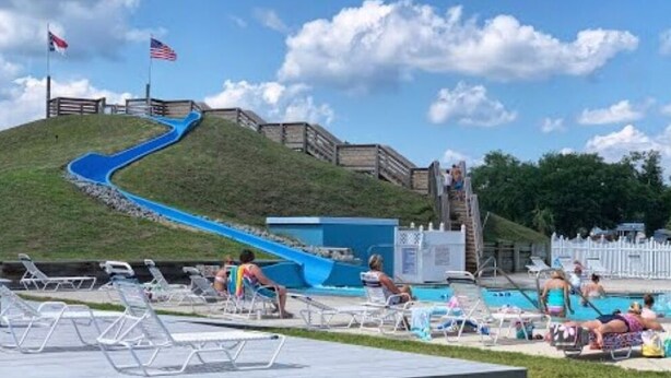 A water slide leading to a pool area with lounge chairs and a flag. - Cozy park model at campground in enchanting Newport NC. (Newport)