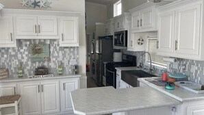 A kitchen with white cabinets, a marble countertop, and a tiled backsplash. - Cozy park model at campground in enchanting Newport NC. (Newport)