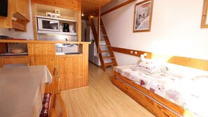 Una habitación pequeña con kitchenette, una cama y una escalera de madera.