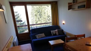 A small room with a blue sofa, a wooden table, a bench, and a window with a view of trees. - 50m from resort center, 14th floor, balcony, tv, 29m², Les Arcs (Les Arcs)