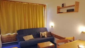 A living room with a dark blue sofa, two wooden chairs, a small wooden table, and a yellow curtain. - 50m from resort center, 14th floor, balcony, tv, 29m², Les Arcs (Les Arcs)