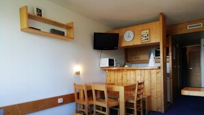 A compact room with a wooden dining table and chairs, a small kitchenette with a microwave, and a television mounted on the wall. - 50m from resort center, 14th floor, balcony, tv, 29m², Les Arcs (Les Arcs)