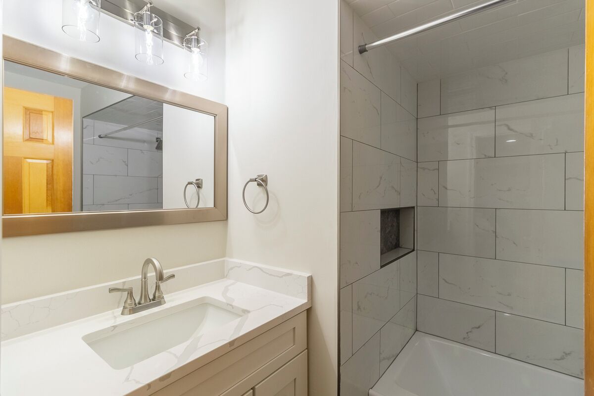 A bathroom with a white sink, a mirror, and a shower area with white tiles.